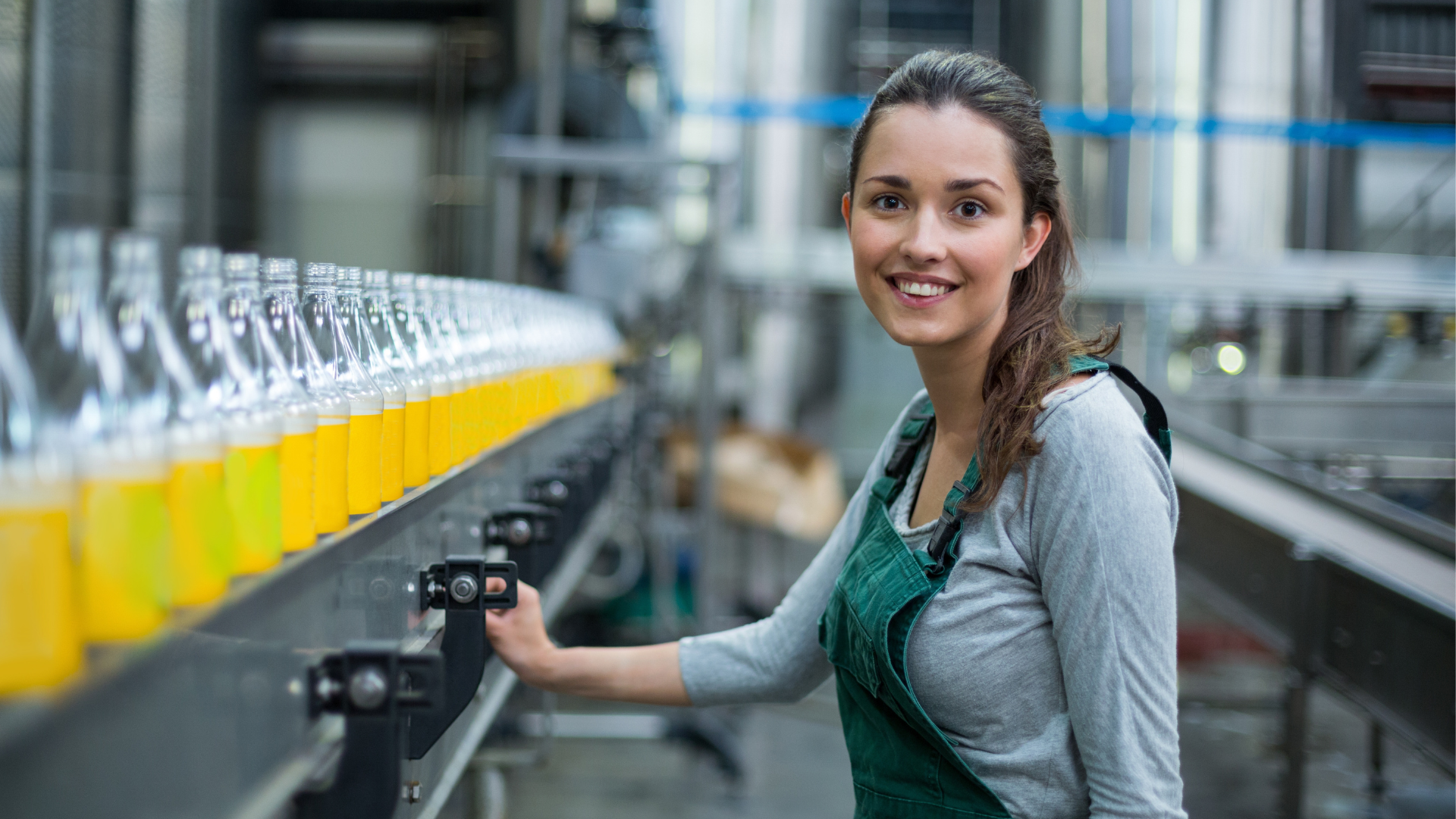 A female factory worker standing near production line at drinks production factory