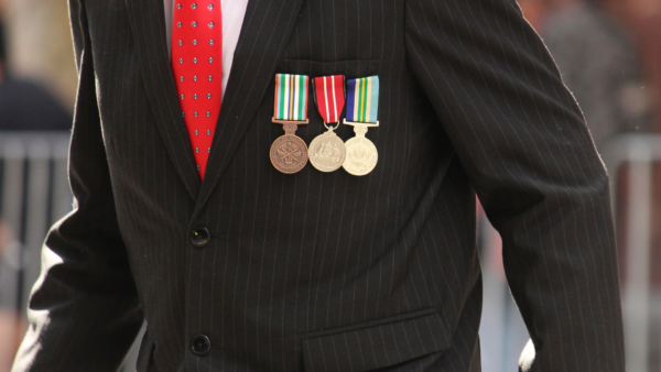 Senior man wearing military medals, suit and tie walking after the Dawn Service at Martin Place during Anzac Day in the City
