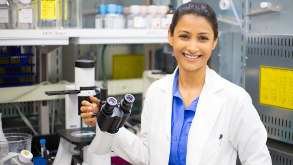 Close portrait of a health and medical researcher standing beside a microscope in an isolated laboratory