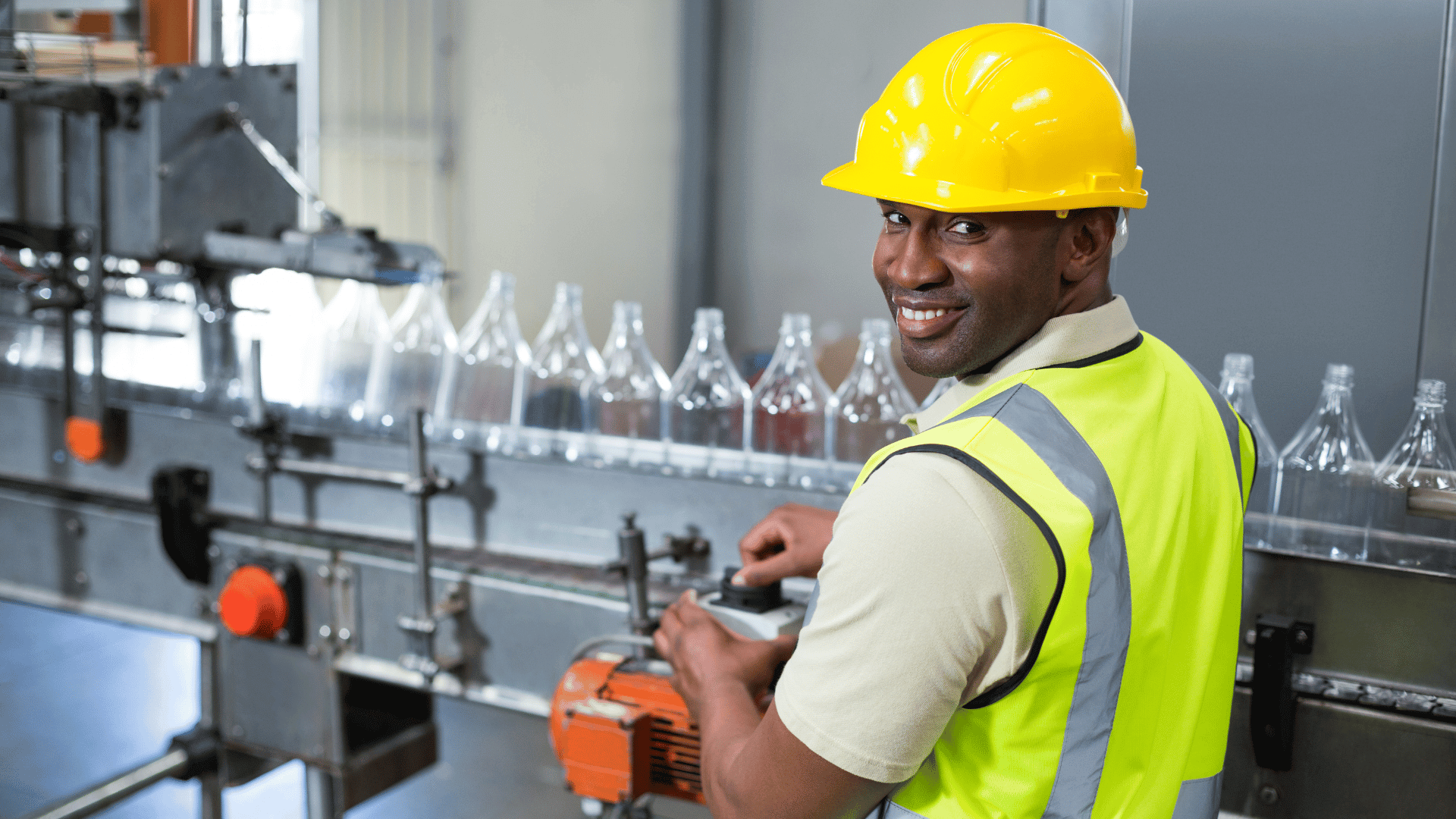 Smiling factory worker operating machine in drinks production plant