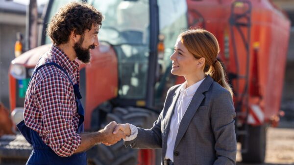 Farmer and businesswoman shaking hands in front of tractor