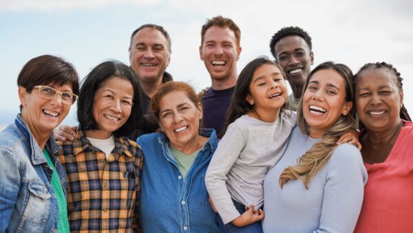Group of multigenerational people hugging each other while smiling on camera