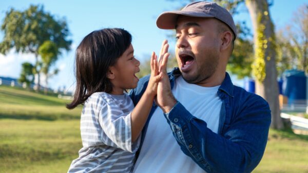 Happy asian boy smiling happy while holding an father hand, enjoying a warm and safe moment together on the park lawn at sunset on weekend.