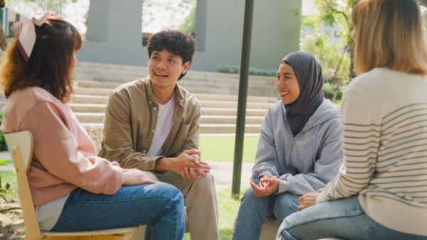 Small Asian group of people sit in a close circle and talk to a therapist in park